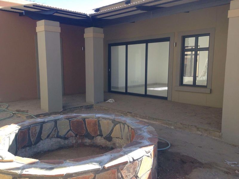 A covered patio area featuring a stone-clad fire pit, concrete pillars, and sliding glass doors leading into the interior living space.