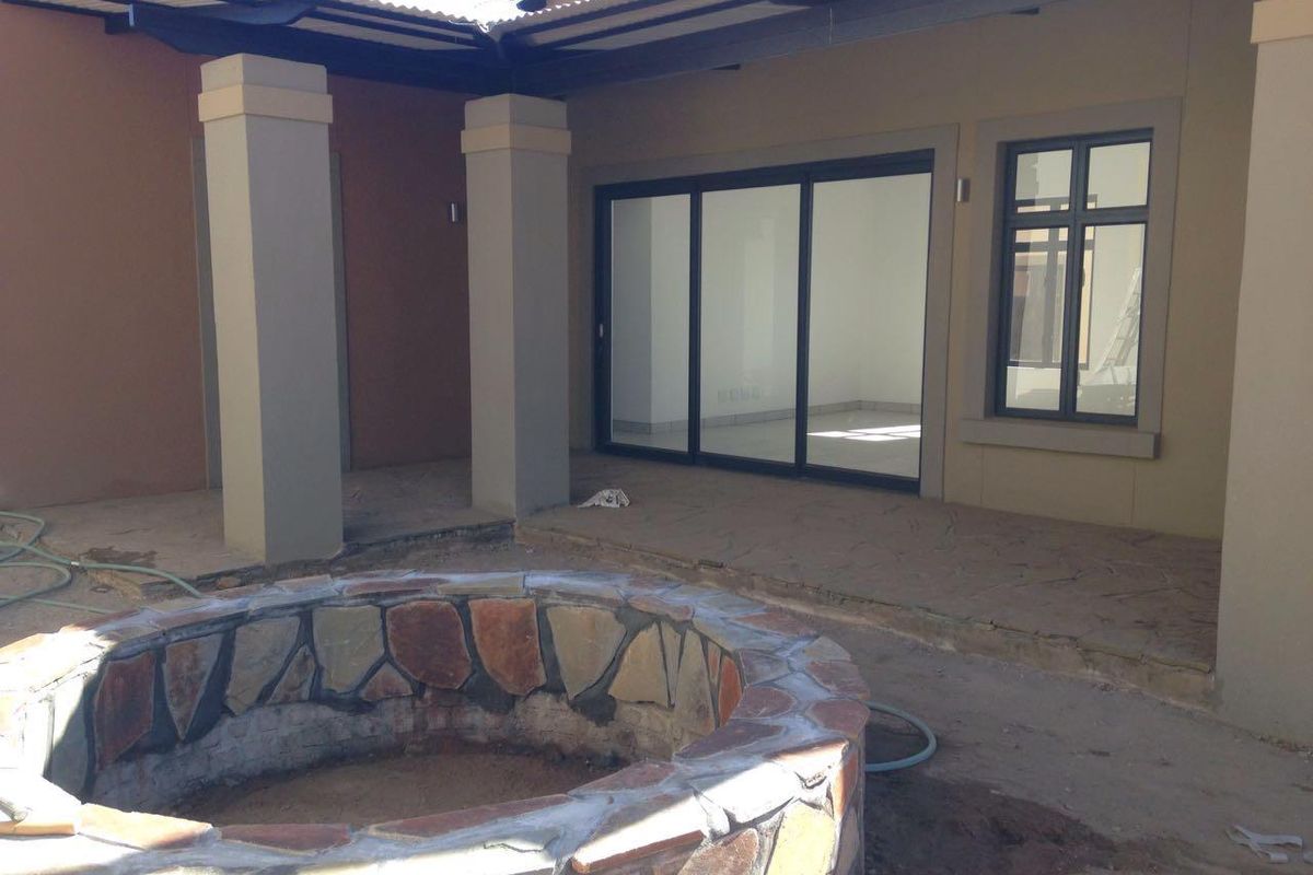 A covered patio area featuring a stone-clad fire pit, concrete pillars, and sliding glass doors leading into the interior living space.