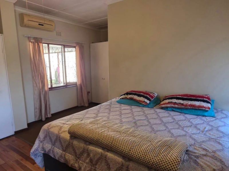A functional bedroom featuring laminate flooring, built-in cupboards, and a wall-mounted air conditioning unit.