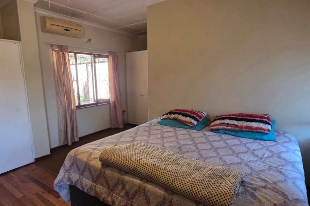 A functional bedroom featuring laminate flooring, built-in cupboards, and a wall-mounted air conditioning unit.