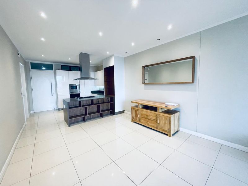 Modern open-plan living area featuring a sleek kitchen with built-in cabinetry, stainless steel appliances, and polished tiled flooring throughout.
