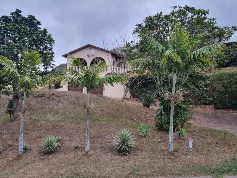 Front elevation of a residential house featuring an arched balcony, paved driveway, and established garden landscaping.