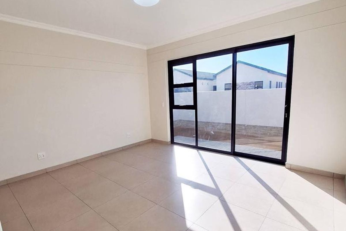A bright, empty living room featuring large black-framed sliding glass doors that provide natural light and direct access to the outdoor area.