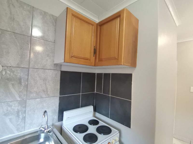 A compact kitchen area featuring built-in wooden cabinetry, a stainless steel sink, and an electric stove with a contrasting tiled splashback.