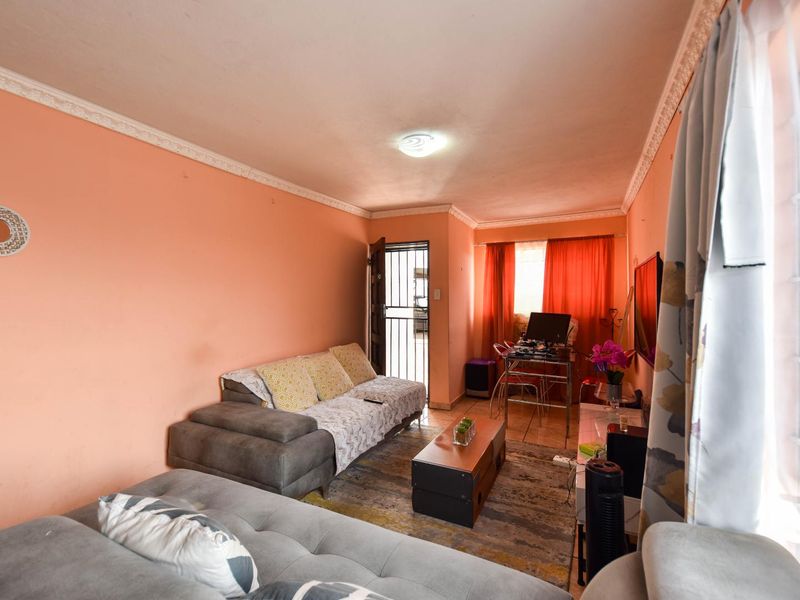 A living room area featuring tiled flooring, decorative ceiling cornices, and a security gate leading to the exterior.