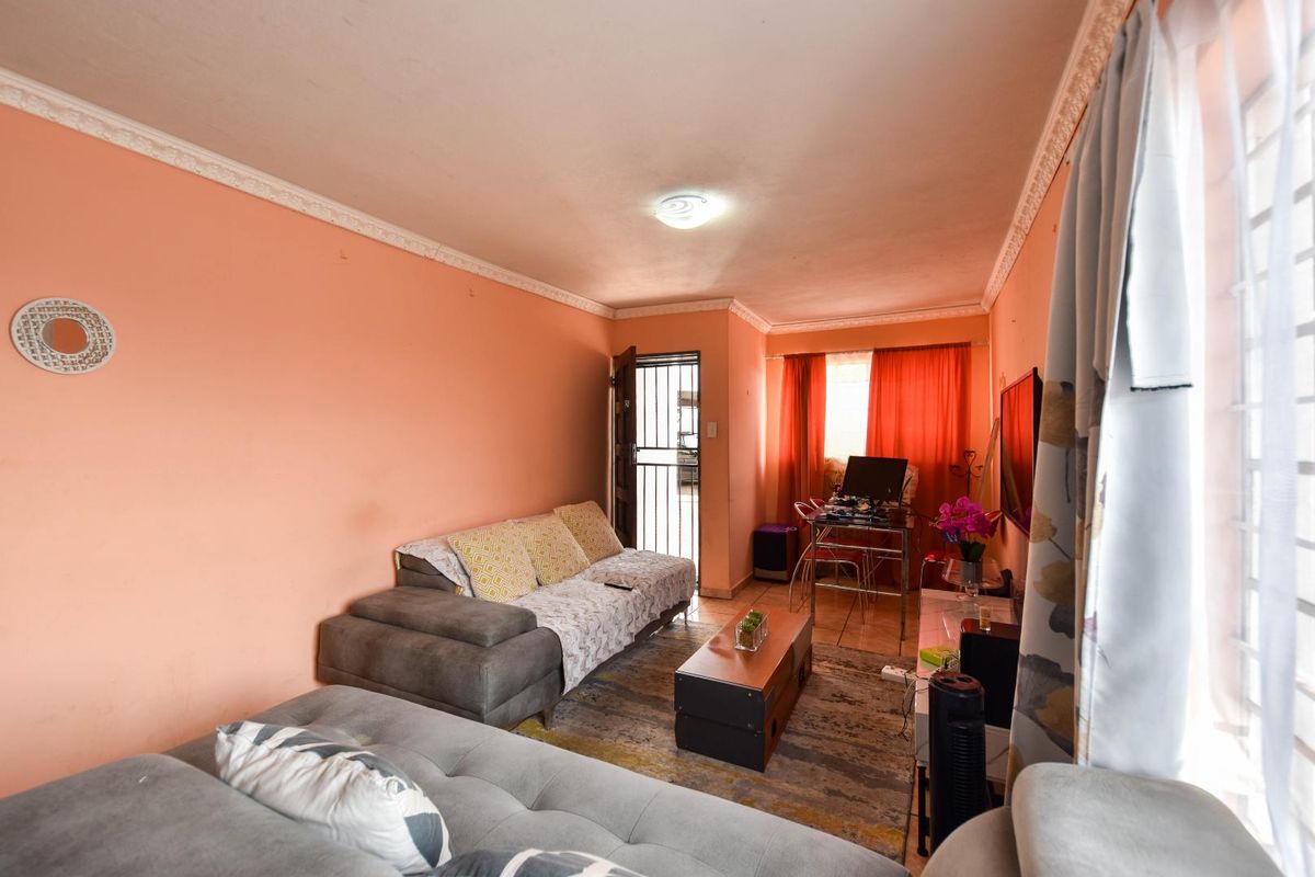 A living room area featuring tiled flooring, decorative ceiling cornices, and a security gate leading to the exterior.