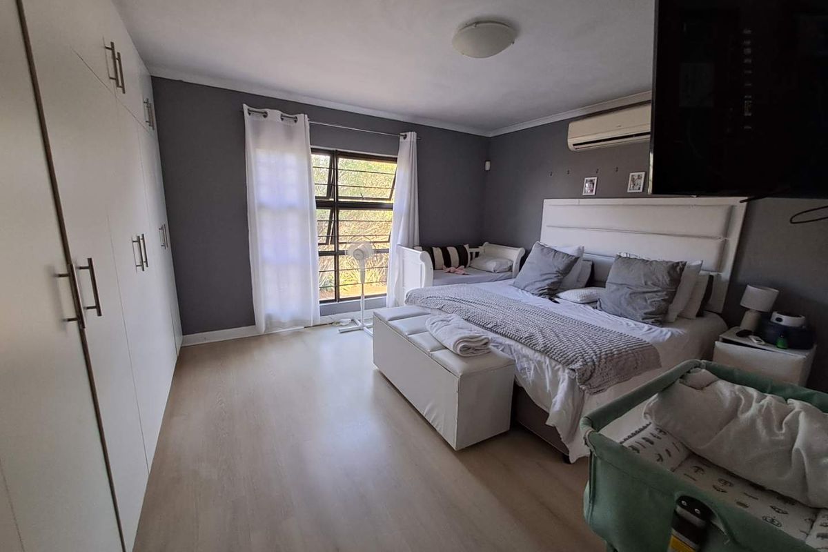 Spacious bedroom featuring built-in cupboards, laminate flooring, and a wall-mounted air conditioning unit.