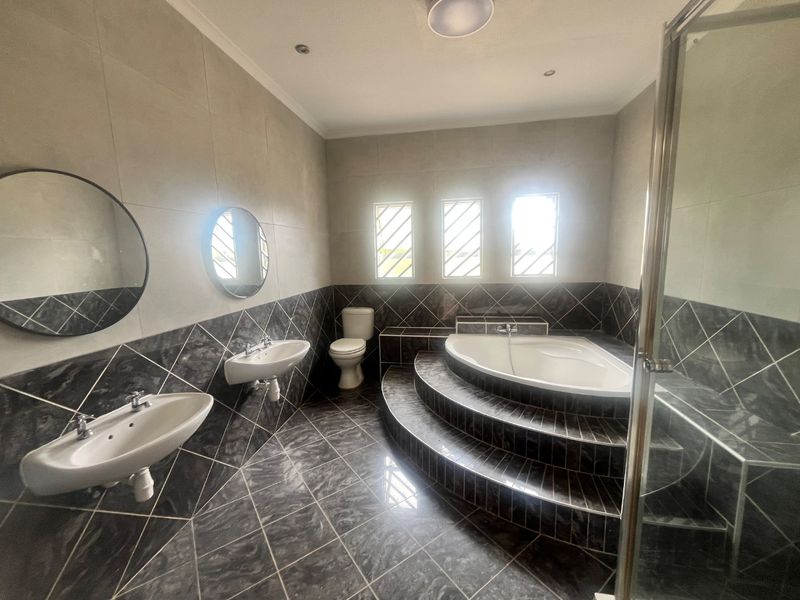 Spacious bathroom featuring a raised platform with a built-in corner bathtub, double wall-mounted basins, a separate shower enclosure, and modern tiled finishes.