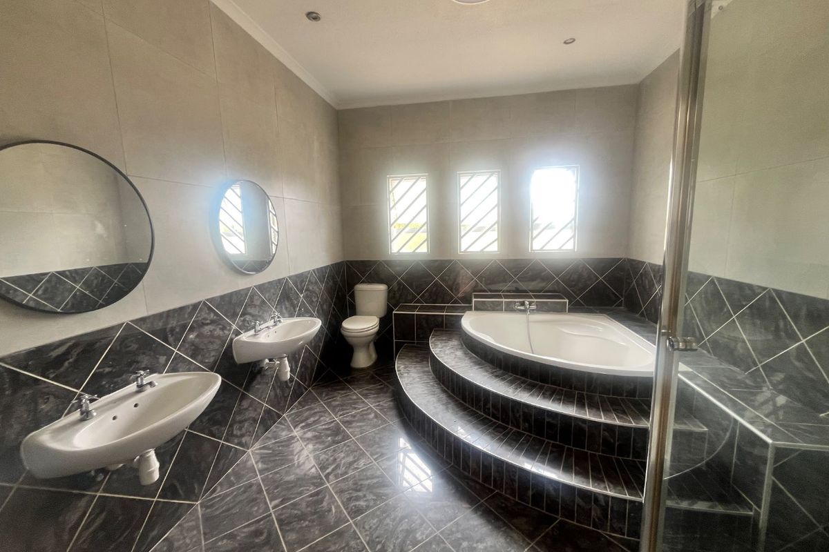 Spacious bathroom featuring a raised platform with a built-in corner bathtub, double wall-mounted basins, a separate shower enclosure, and modern tiled finishes.