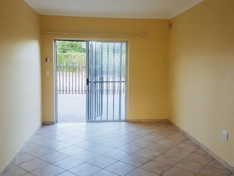 An empty living room featuring tiled flooring and a sliding glass door with a security gate, providing direct access to the exterior.
