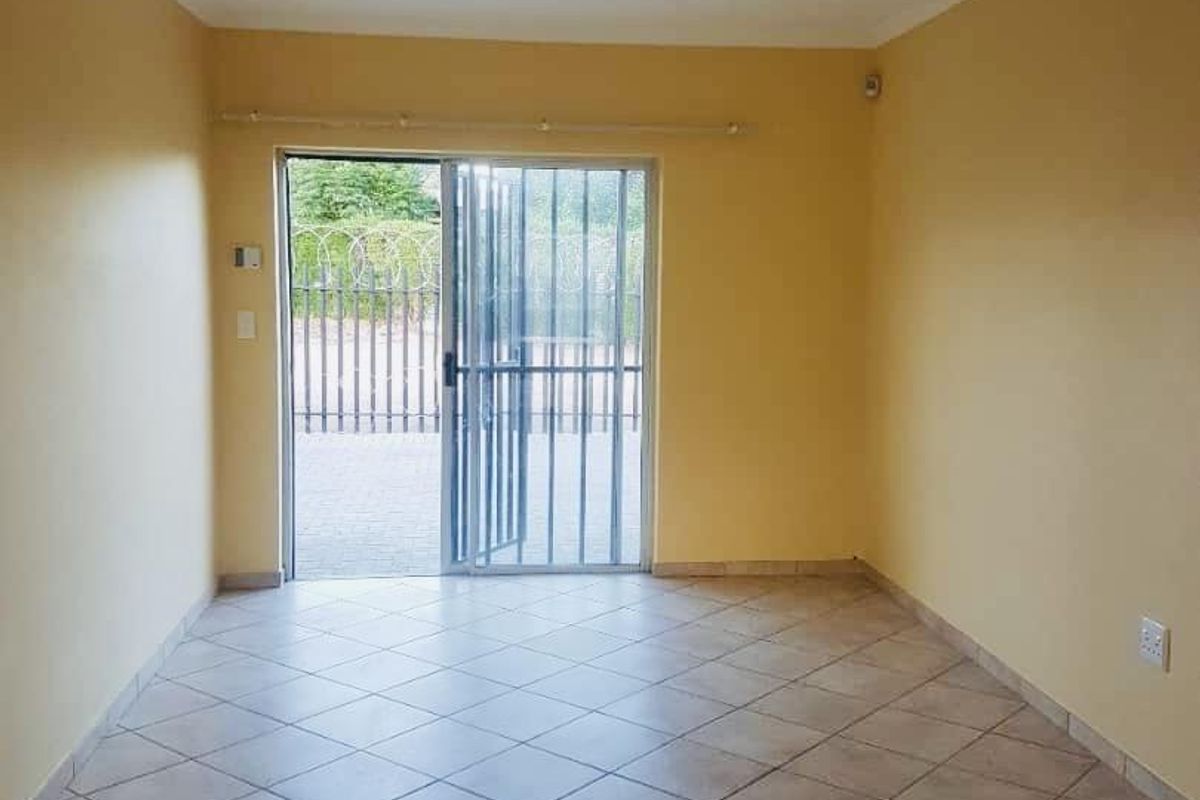 An empty living room featuring tiled flooring and a sliding glass door with a security gate, providing direct access to the exterior.