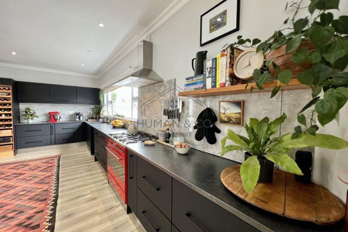 Modern kitchen featuring matte black cabinetry, stone-look splashback, integrated stainless steel extractor fan, and a striking red freestanding oven.