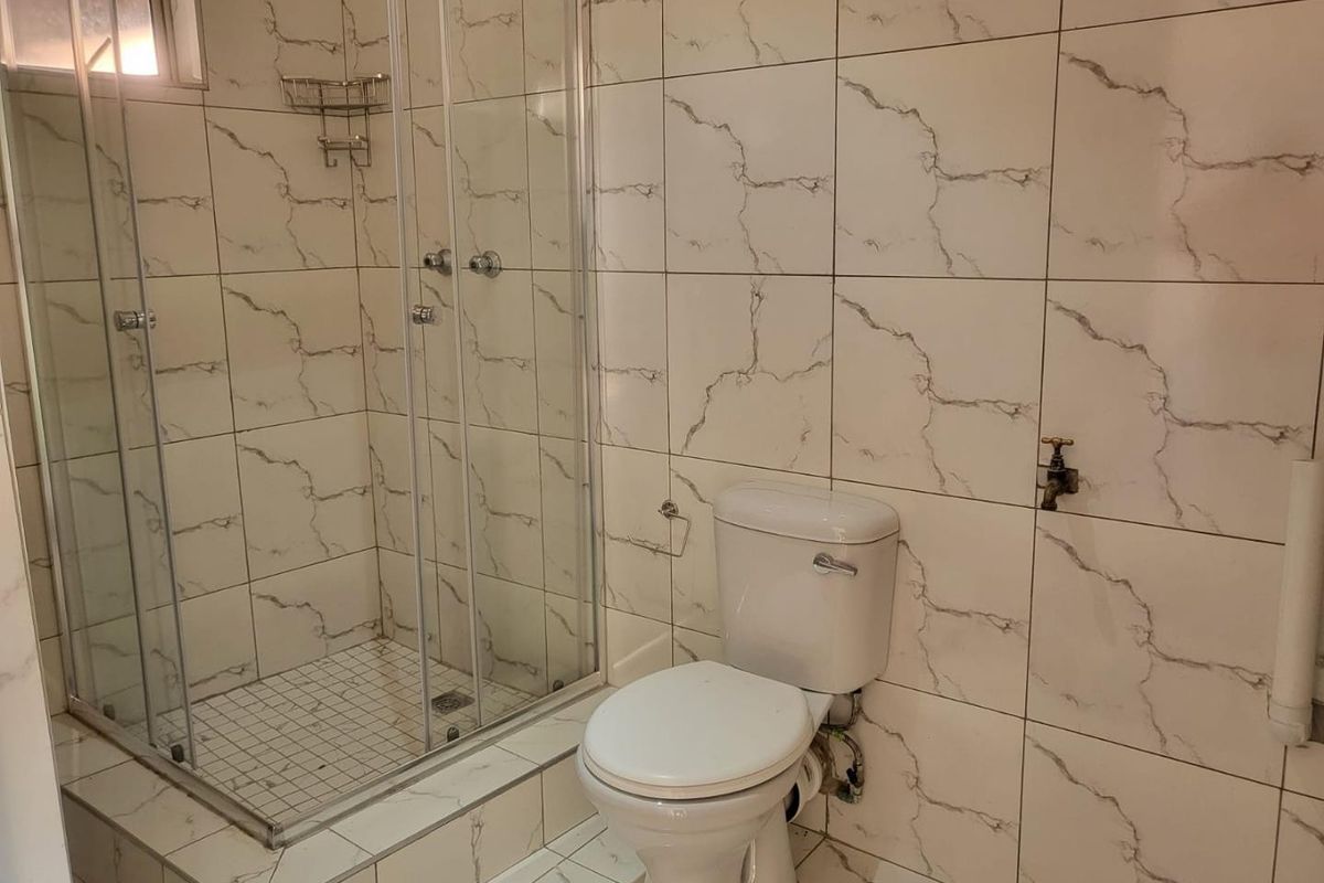 A functional bathroom featuring a glass shower enclosure, toilet, and marble-look tiled walls and flooring.