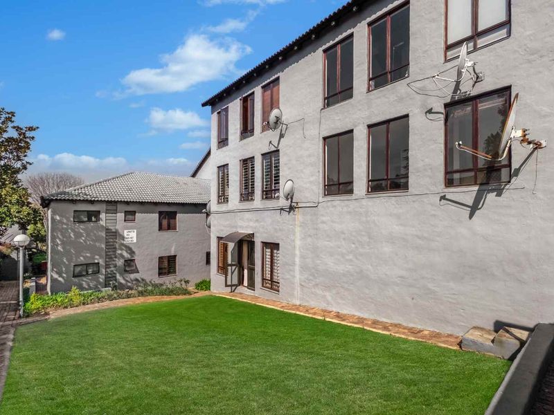 Rear view of the apartment complex featuring a shared lawn area, paved pathways, and multi-story building facade with multiple satellite dish installations.