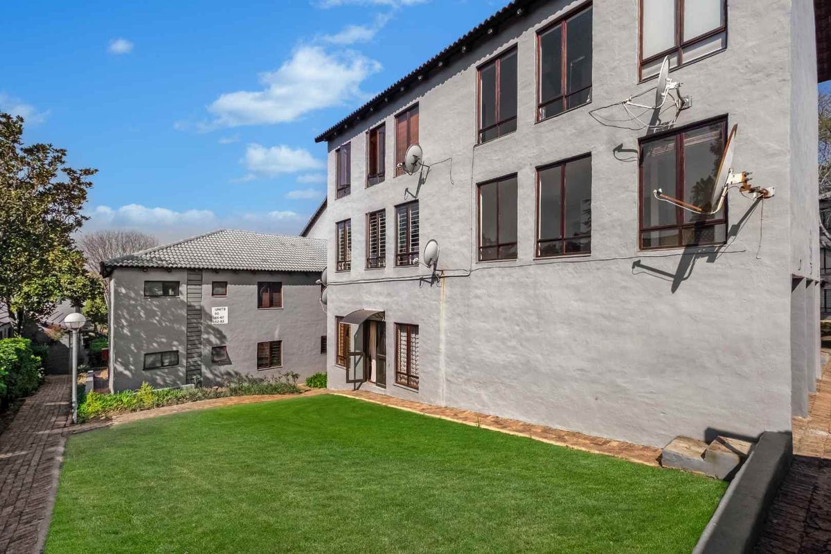 Rear view of the apartment complex featuring a shared lawn area, paved pathways, and multi-story building facade with multiple satellite dish installations.