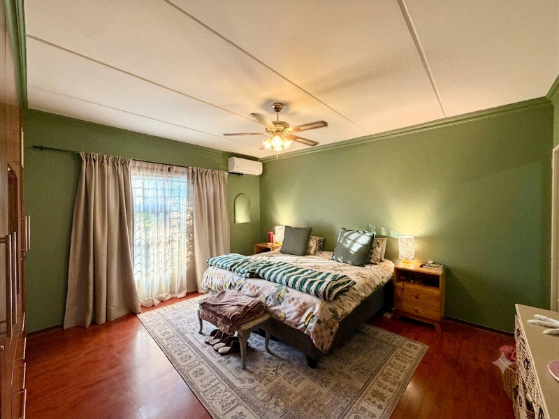 A spacious bedroom featuring laminate flooring, a ceiling fan, and a wall-mounted air conditioning unit, offering a comfortable and functional living space.