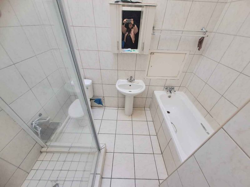 A functional bathroom featuring a pedestal basin, bathtub, and separate glass shower enclosure with full-height wall tiling.