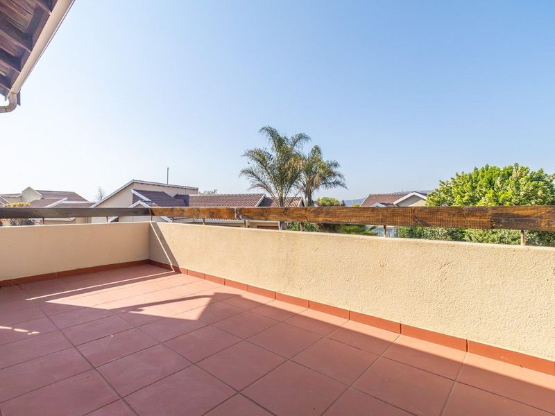 An open-air balcony featuring tiled flooring and a masonry balustrade with a timber handrail, offering an elevated view of the surrounding townhouse complex.