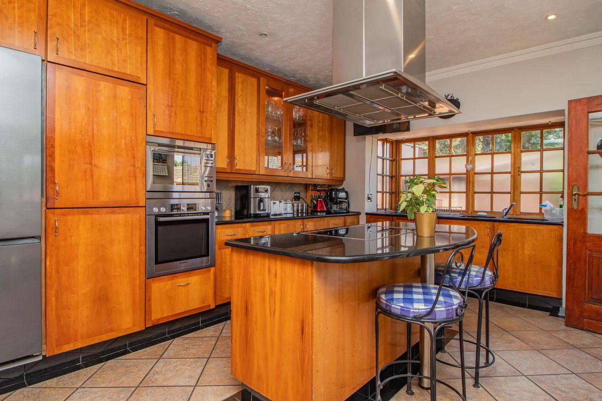 A traditional kitchen featuring warm-toned wooden cabinetry, a central island with a black granite countertop, and a stainless steel extractor fan.