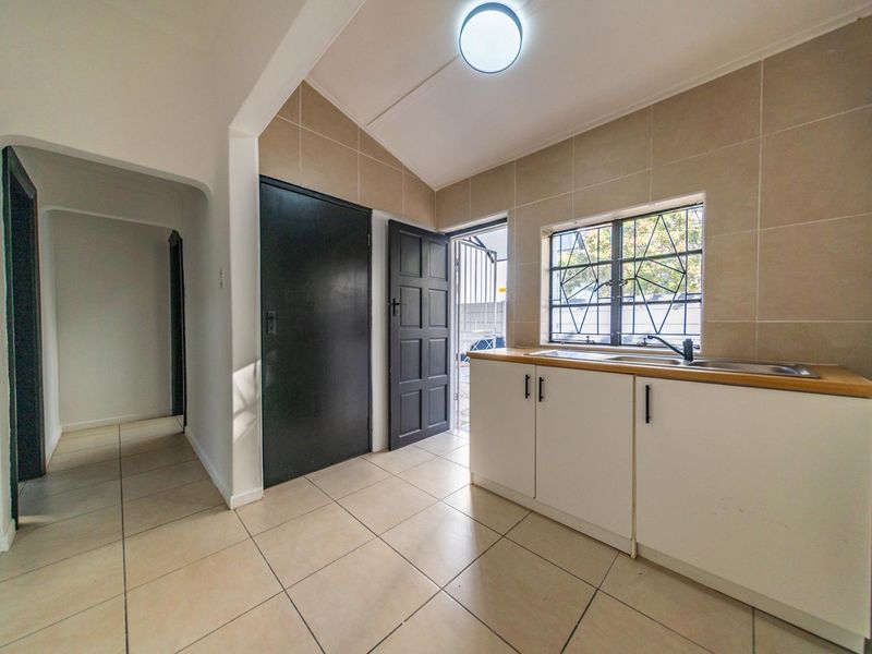 A functional kitchen area featuring tiled flooring, neutral wall tiles, built-in cabinetry with a stainless steel sink, and direct access to an outdoor area.