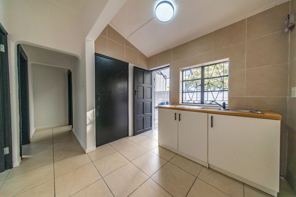 A functional kitchen area featuring tiled flooring, neutral wall tiles, built-in cabinetry with a stainless steel sink, and direct access to an outdoor area.