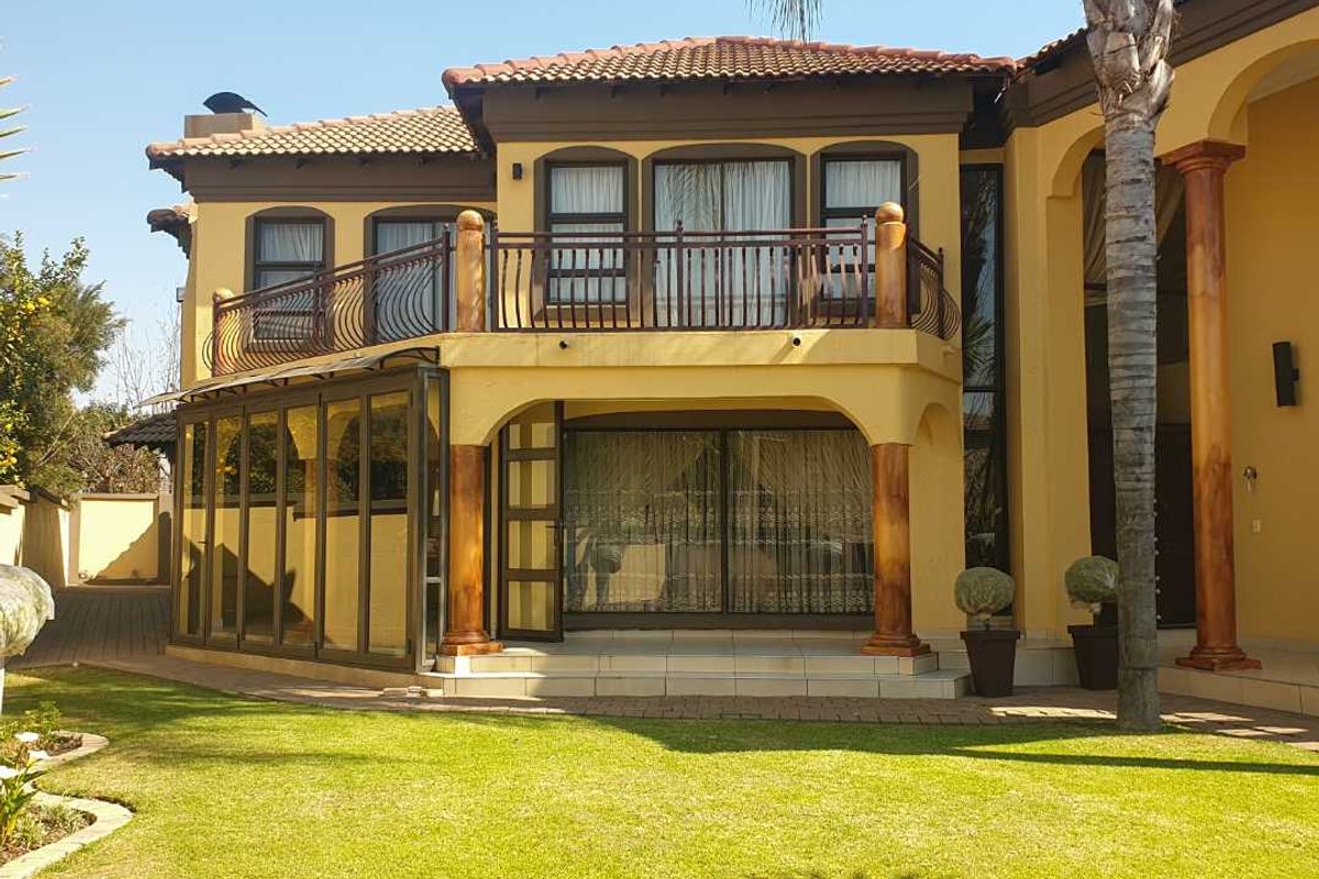Rear view of a multi-story residence featuring a covered patio, an enclosed sunroom, and an upper-level balcony with decorative columns and wrought iron railings.