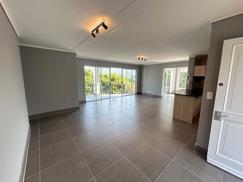Spacious open-plan living and kitchen area featuring large sliding doors, modern tiled floors, and neutral grey walls with integrated lighting.