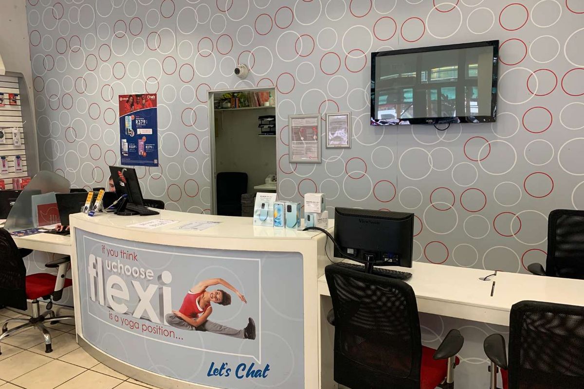 A retail service counter area featuring a curved reception desk, tiled flooring, and wall-mounted display screen in a commercial setting.