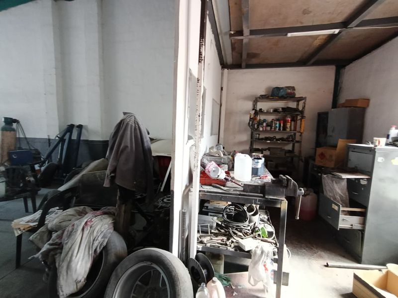 Industrial utility or workshop space featuring a metal workbench, fixed shelving, and exposed ceiling structure, suitable for storage or light industrial operations.