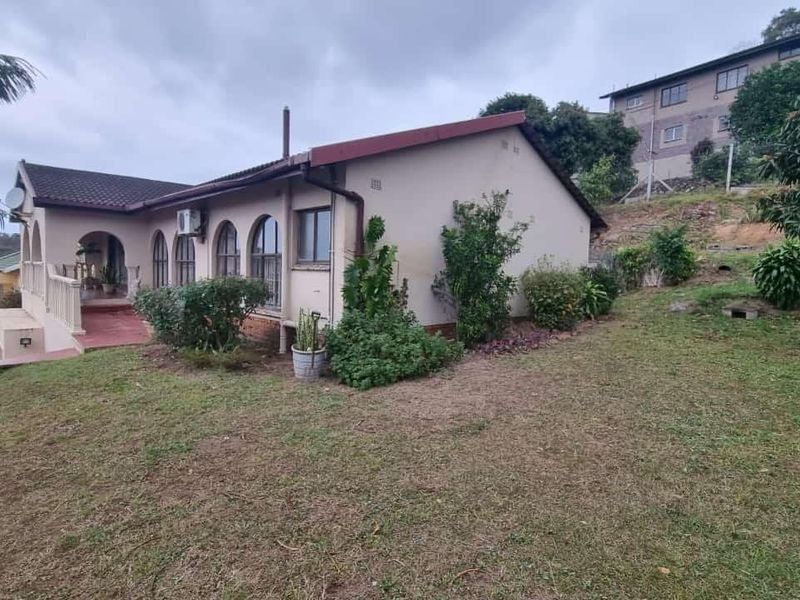 Rear view of the house featuring a covered veranda, arched windows, and a spacious garden area.