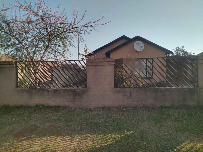 Front view of a residential house featuring a perimeter wall with metal security fencing and a satellite dish mounted on the exterior wall.