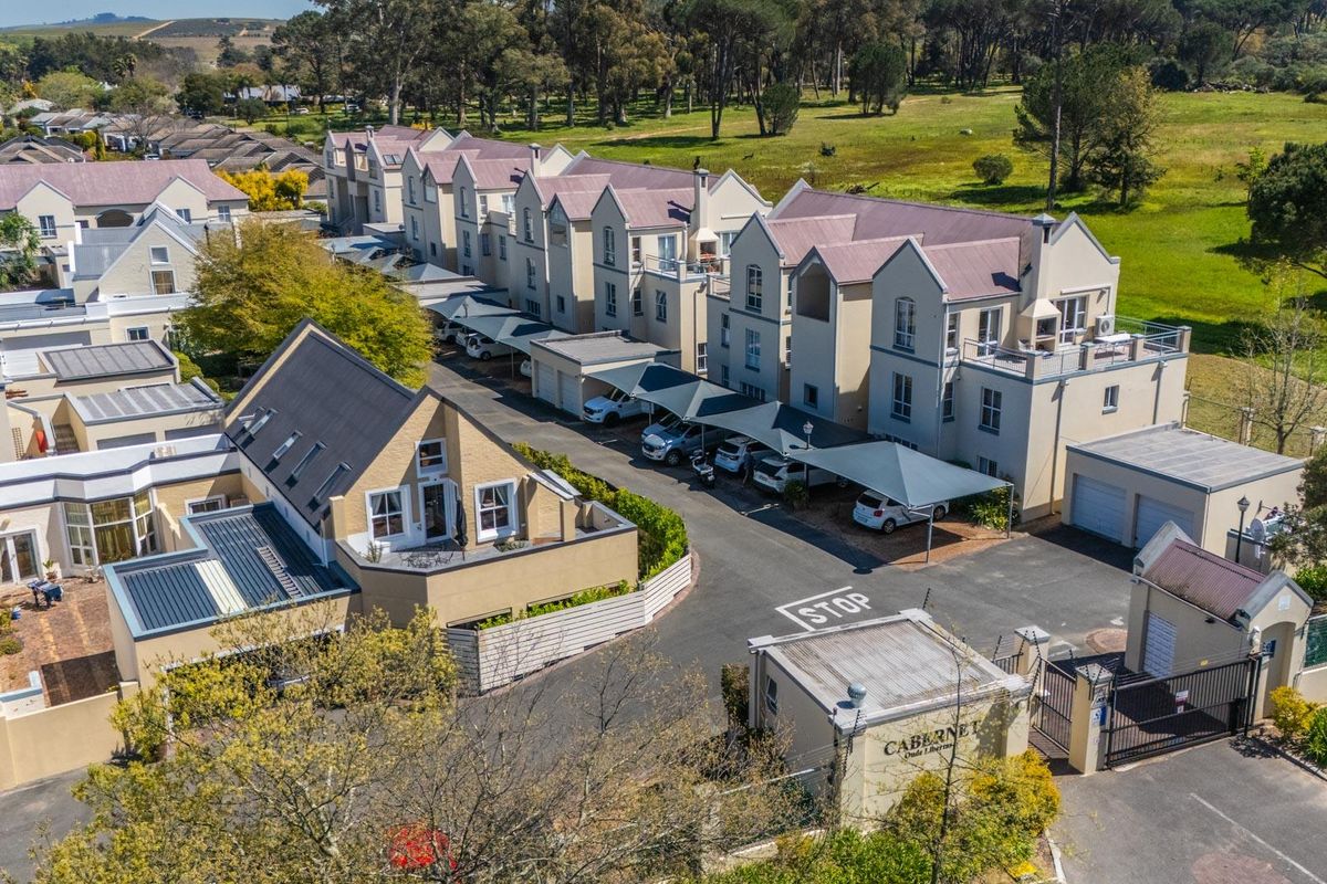 Aerial view of a residential apartment complex featuring paved driveways, covered parking bays, and a secure gated entrance.