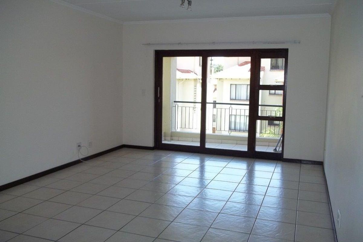 An empty living room featuring neutral floor tiles, white walls, and large sliding glass doors providing access to a private balcony.