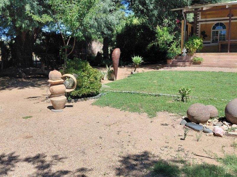 A spacious garden area featuring a manicured lawn, gravel pathways, mature trees, and a view of the home's covered patio.
