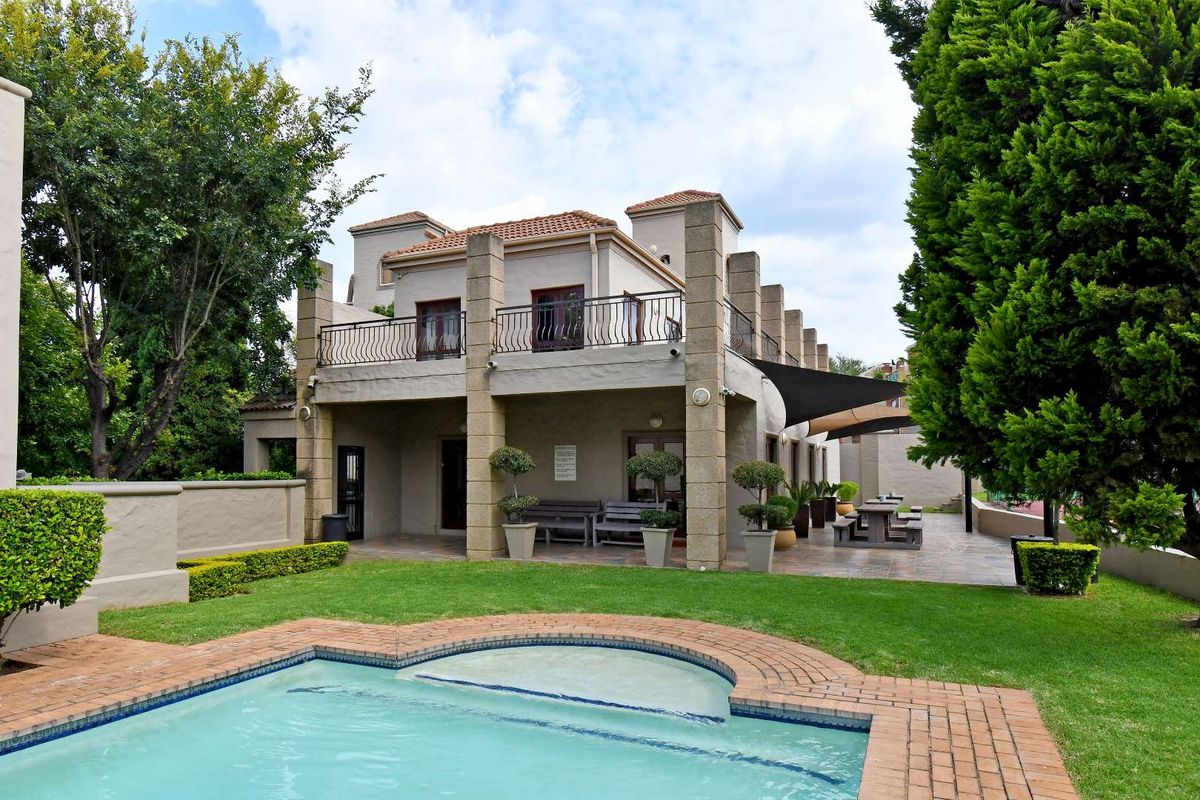 Rear view of the apartment building featuring a swimming pool, landscaped garden, and a spacious tiled patio with a balcony above.