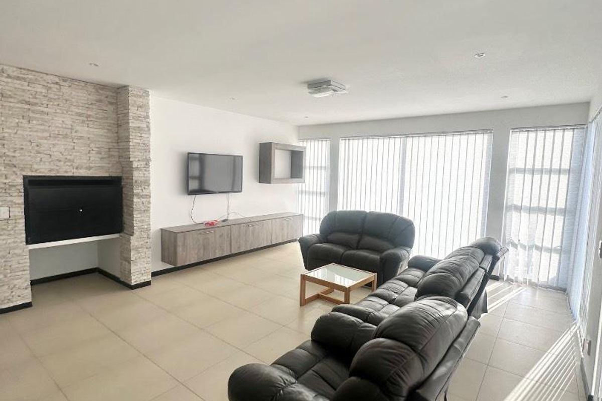 Spacious living room featuring large format floor tiles, a stone-clad fireplace feature wall, and floor-to-ceiling windows with vertical blinds.