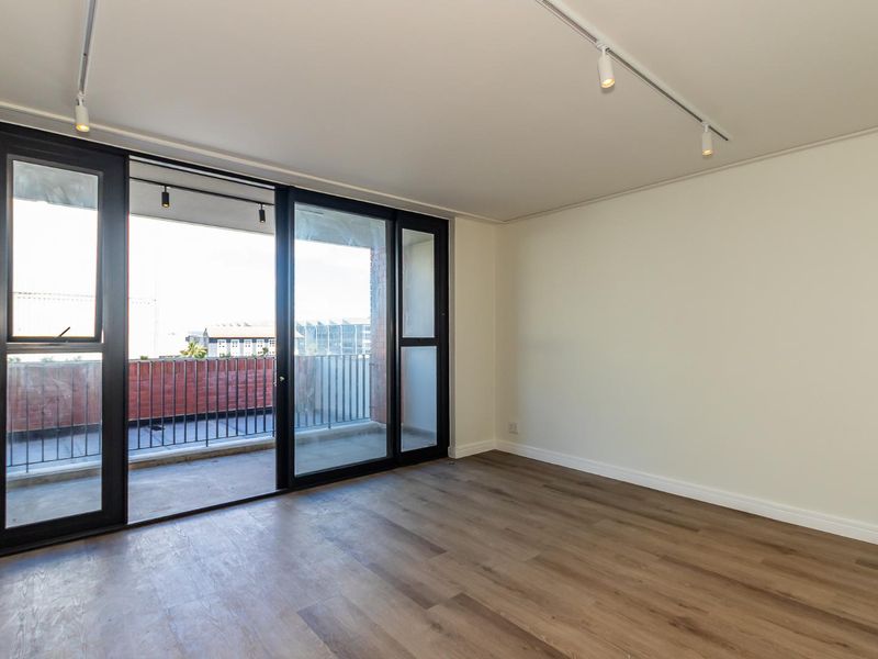 Bright and spacious living area featuring modern laminate flooring, track lighting, and large sliding glass doors leading to a private balcony.