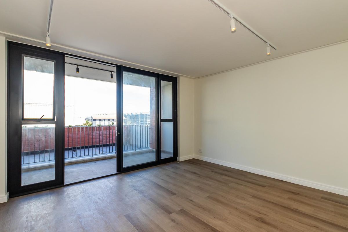 Bright and spacious living area featuring modern laminate flooring, track lighting, and large sliding glass doors leading to a private balcony.