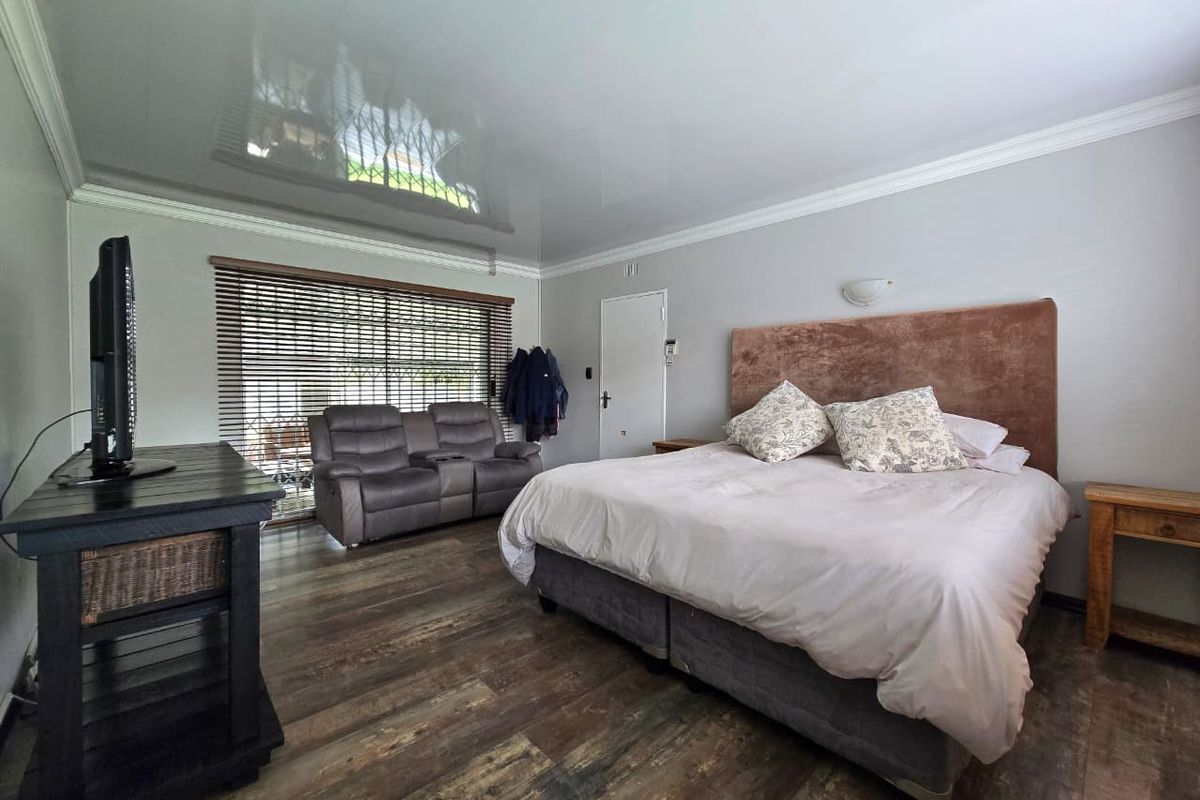 Spacious bedroom featuring wood-look flooring, a glossy ceiling finish, and large windows with fitted blinds, providing a comfortable and functional living space.