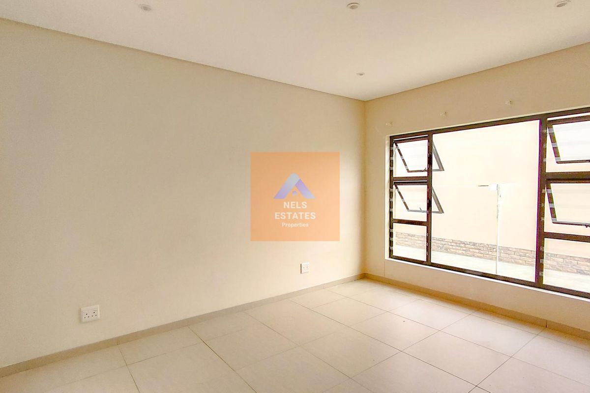 A bright, empty bedroom featuring neutral tiled flooring, recessed downlights, and large aluminium-framed windows providing natural light.