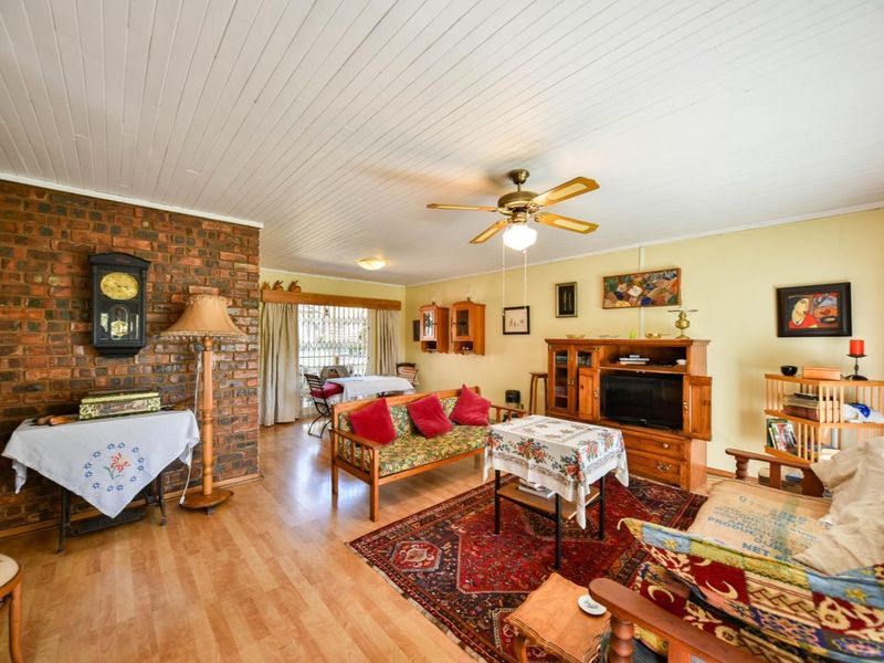 A living room featuring an exposed brick feature wall, timber tongue and groove ceiling, ceiling fan, and laminate flooring.