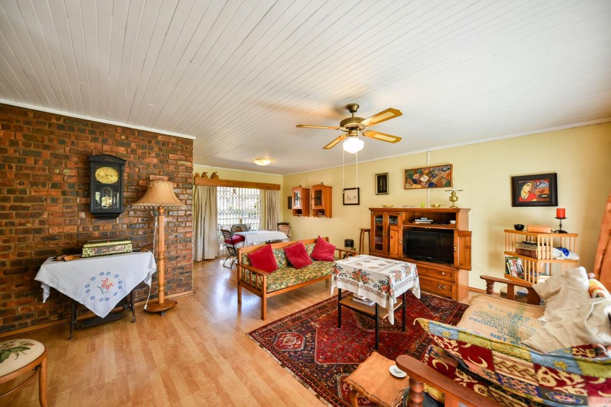 A living room featuring an exposed brick feature wall, timber tongue and groove ceiling, ceiling fan, and laminate flooring.