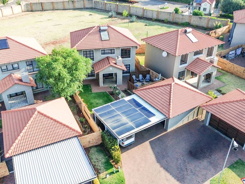 Aerial view of a residential estate featuring multiple homes with tiled roofs, solar panels, solar geysers, and paved driveways.