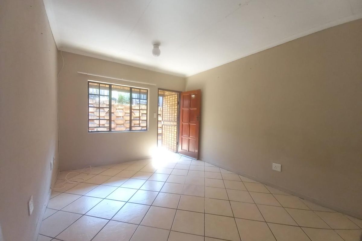 An empty living room featuring neutral wall paint, tiled flooring, a security gate, and a wooden entrance door.