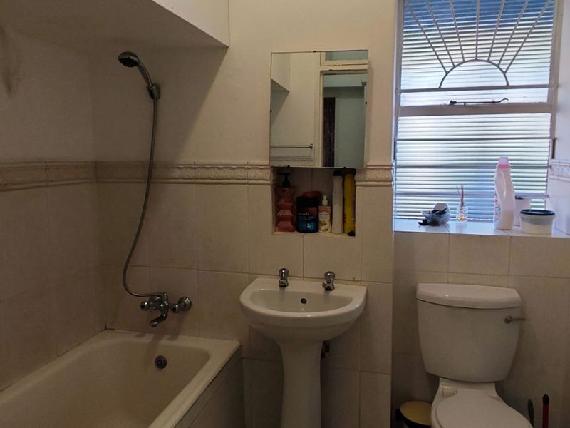 A dated bathroom featuring a bathtub with shower mixer, pedestal basin, toilet, and tiled walls with a recessed storage niche.