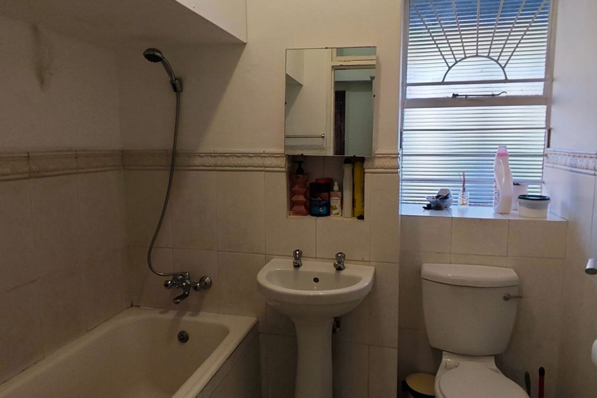 A dated bathroom featuring a bathtub with shower mixer, pedestal basin, toilet, and tiled walls with a recessed storage niche.