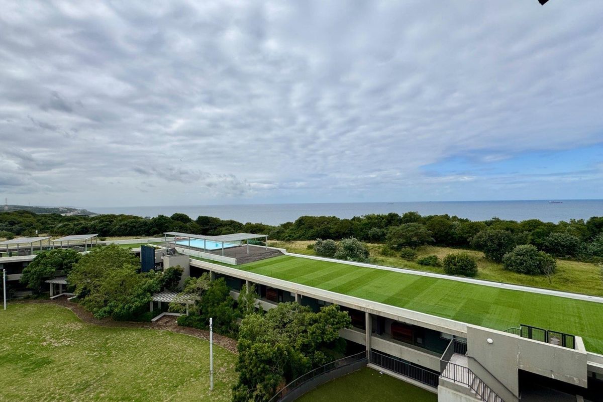 Aerial view of a modern apartment complex featuring a green roof, rooftop swimming pool, and landscaped grounds with ocean views.