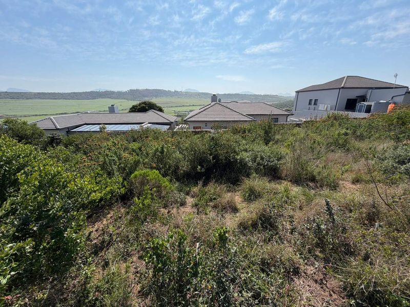 A view of the vacant residential land featuring natural vegetation and a sloped landscape with surrounding residential properties in the distance.
