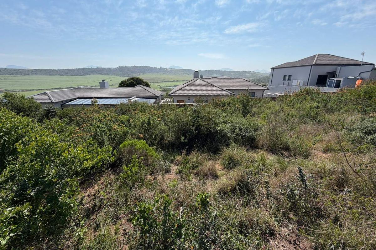 A view of the vacant residential land featuring natural vegetation and a sloped landscape with surrounding residential properties in the distance.