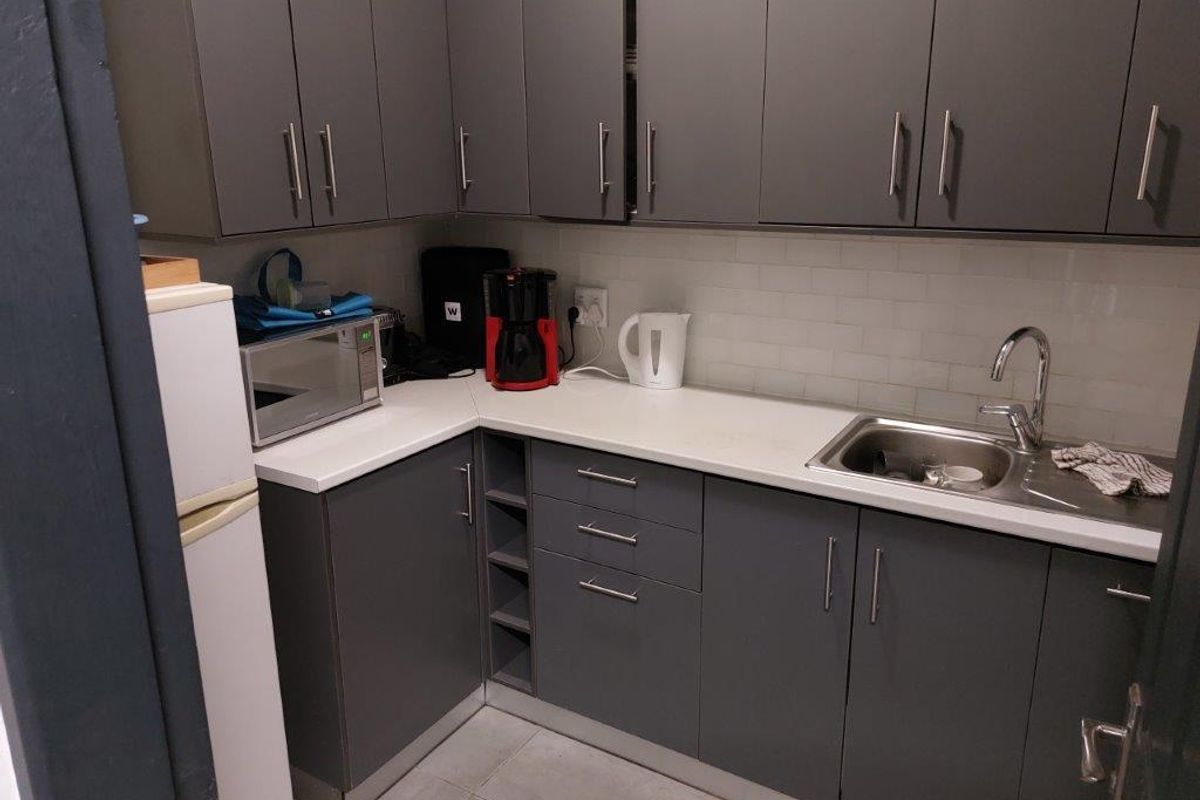 A compact kitchen area featuring modern grey cabinetry, white countertops, a stainless steel sink, and a tiled backsplash.